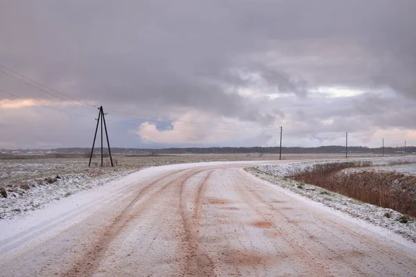 覆盖着白雪的乡间小路穿过田野 变压器杆 从车上俯瞰全景 五彩斑斓的云彩 戏剧性的日落 冬季轮胎 偏远村庄 — 图库照片