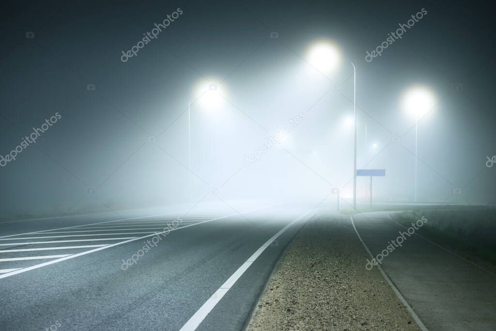 Panoramic view of the illuminated new highway in a fog at night, street lights close-up. Moonlight. Dark urban scene. Europe. Transportation, logistics, travel, tourism, road trip, freedom, driving