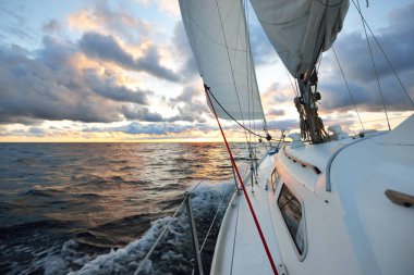 Gün batımında açık denizde yelken açmak. Güvertenin yakın görüntüsü, direk ve yelkenler. Yağmurdan sonra açık gökyüzü, çarpıcı parlayan bulutlar, altın güneş ışığı, dalgalar ve su sıçramaları, kasırga. Destansı deniz manzarası