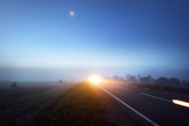 Gece sisli bir havada boş otobanın panoramik görüntüsü. Ay ışığı. Gün doğumu. Avrupa. Ulaşım, lojistik, seyahat, yolculuk, özgürlük, sürüş. Hareket bulanıklığı etkisi. Kırsal alan