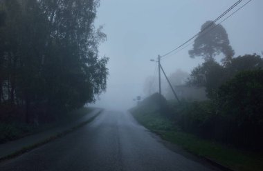 Yağmurlu bir sonbahar gününde, karanlık fırtınalı bir gökyüzünde, ağaçların ve köyün arasında asfalt bir yol. Yolculuk, ulaşım, iletişim, sürüş
