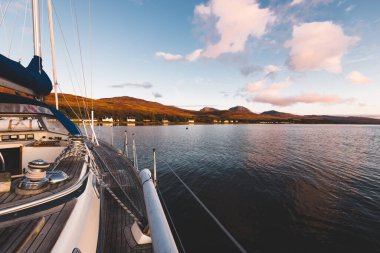 Günbatımında Jura adasının kayalık kıyılarında seyir halindeki ahşap meşe güvertesiyle donatılmış modern bir yat. Inner Hebrides, İskoçya, İngiltere. Spor, eğlence, gezi, seyahat yerleri.