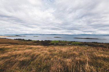 Jura adasının kıyıları, dağları ve vadilerinin panoramik hava manzarası. Bulutlu mavi gökyüzü. Fırtınalı hava. Paps of Jura, Inner Hebrides, İskoçya, İngiltere. Seyahat yerleri, turizm, ulusal simgeler