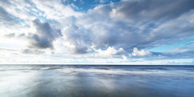 Gün batımında fırtınadan sonra Baltık kıyıları üzerinde parlayan kümülüs bulutlarıyla açık bir gökyüzü. Dramatik bulut manzarası. Resimli bir manzara var. Kararsız hava, iklim değişikliği. Uzun pozlama