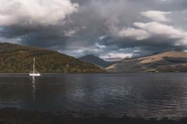 Yelkenli tekneleri Loch Fyne kıyısında demirlemiş, yakın mesafeden. Dramatik bir gökyüzü. Arkadaki görkemli orman tepeleri. Inveraray, Argyll ve Bute, İskoçya, İngiltere. Seyahat hedefleri teması