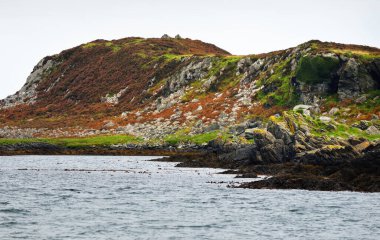 Jura adasının kıyılarının panoramik manzarası, dağları ve vadileri sudan. Bulutlu mavi gökyüzü. Fırtınalı hava. Paps of Jura, Inner Hebrides, İskoçya, İngiltere