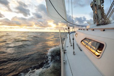 Gün batımında açık denizde yelken açmak. Güvertenin yakın görüntüsü, direk ve yelkenler. Yağmurdan sonra açık gökyüzü, çarpıcı parlayan bulutlar, altın güneş ışığı, dalgalar ve su sıçramaları, kasırga. Destansı deniz manzarası