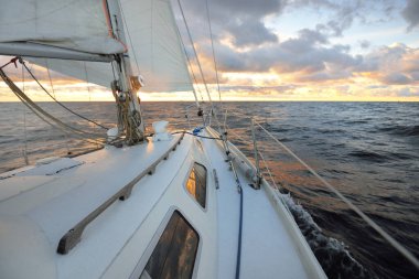 Gün batımında açık denizde yelken açmak. Güvertenin yakın görüntüsü, direk ve yelkenler. Yağmurdan sonra açık gökyüzü, çarpıcı parlayan bulutlar, altın güneş ışığı, dalgalar ve su sıçramaları, kasırga. Destansı deniz manzarası