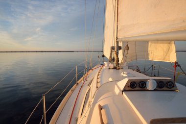 Günbatımında yağmurdan sonra beyaz yat denize açılacak. Güverteden pruvaya kadar yakın çekim. Durgun bir suya yansıyan parlak bulutlarla dolu berrak mavi bir gökyüzü. Idyllic deniz manzarası. Deniz, seyahat, seyahat yerleri