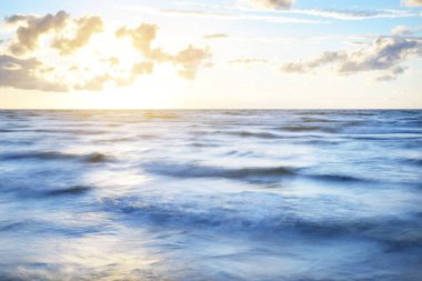 Gök gürültülü fırtınadan sonra denizin üstünde destansı, parlak, altın renkli günbatımı bulutları. Dramatik bir gökyüzü. Dalgalar ve su dokuya sıçrar. Idyllic deniz manzarası. Kavramsal görüntü, uzun pozlama. Resim gibi bir manzara.