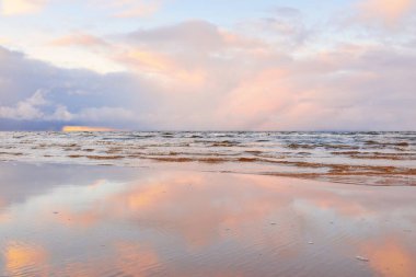 Kumlu bir sahilden Baltık Denizi 'nin panoramik manzarası. Açık günbatımı gökyüzü, parlak pembe bulutlar, yumuşak ışık. Suyun simetri yansımaları, doğal ayna. Hava, kış, iklim değişikliği, doğa