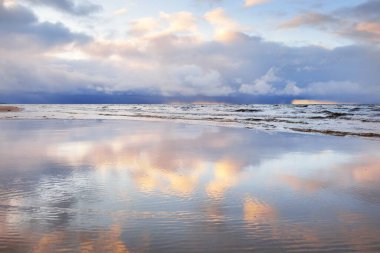 Kumlu bir sahilden Baltık Denizi 'nin panoramik manzarası. Açık günbatımı gökyüzü, parlak pembe bulutlar, yumuşak ışık. Suyun simetri yansımaları, doğal ayna. Hava, kış, iklim değişikliği, doğa