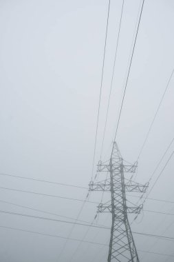 Elektrik hattının siluetleri kalın bir sis tabakasında, yakın plan. Şehir manzarası, manzara. Enerji, enerji üretimi, özel ekipman, endüstri, çevresel hasar, ekoloji, altyapı