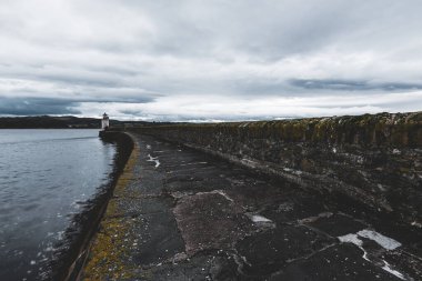 Eski deniz fenerine doğru boş bir gezinti, yakın plan. Arka planda kayalık kıyılar var. Dramatik bulut manzarası. Ardrishaig, Crinan Kanalı, İskoçya, İngiltere. Seyahat yerleri, gezi teması