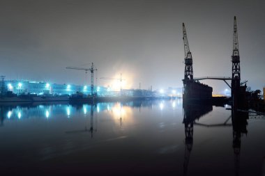 Kargo limanı terminali ve nehir gece. Gemi, vinç, depo. Aydınlatılmış Noel ağacı, arka planda ışıklar. Karanlık şehir manzarasını kavra. Sudaki simetri yansımaları