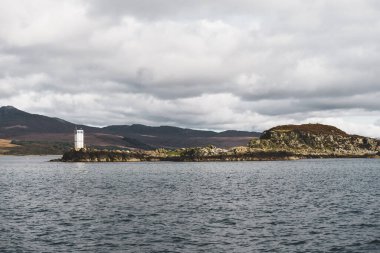 Fırtınalı günbatımı gökyüzünün altında dağ tepeleri (Paps of Jura) yakınlarındaki vadinin panoramik manzarası. Beyaz deniz feneri yakın plan. Dramatik bulut manzarası. Craighouse, Inner Hebrides, İskoçya, İngiltere