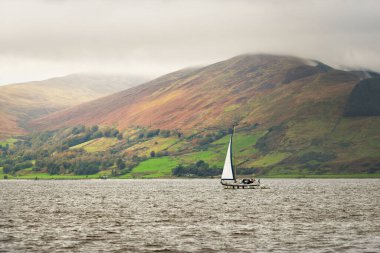 Karanlık fırtına gökyüzü. Bulutlu bir günde yelkenli teknesi olan bir tekne. Bute 'un kayalık kıyılarının sudan panoramik görüntüsü. Tepeler ve dağlar arka planda. Bute Adası, Clyde Firth, İskoçya, İngiltere