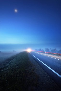 Gece sisli bir havada boş otobanın panoramik görüntüsü. Ay ışığı, temiz gökyüzü. Gün doğumu. Avrupa. Ulaşım, lojistik, seyahat, yolculuk, özgürlük, sürüş. Kırsal alan