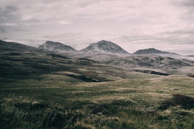 Karanlık fırtına gökyüzünün altındaki Paps of Jura 'nın (Beinn an ir) en yüksek dağı yakınındaki vadinin panoramik manzarası. Dramatik bulutlar. Jura Adası, Inner Hebrides, İskoçya, İngiltere. Atmosferik manzara.