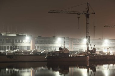 Kargo limanı terminali ve nehir gece. Gemi, vinç, depo. Aydınlatılmış Noel ağacı, arka planda ışıklar. Karanlık şehir manzarasını kavra. Sudaki simetri yansımaları