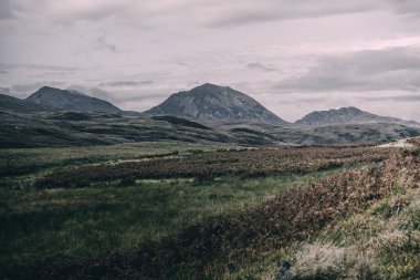 Karanlık fırtına gökyüzünün altındaki Paps of Jura 'nın (Beinn an ir) en yüksek dağı yakınındaki vadinin panoramik manzarası. Dramatik bulutlar. Jura Adası, Inner Hebrides, İskoçya, İngiltere. Atmosferik manzara.