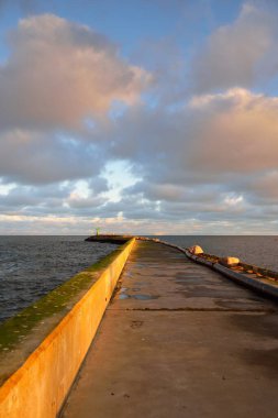 Gün batımında deniz fenerine gidin. Baltık Denizi, Letonya. Dramatik gökyüzü, parlayan bulutlar. Hava, iklim değişikliği, doğa, kış, mevsimler. Noel tatilleri, yerel turizm, tatil beldeleri