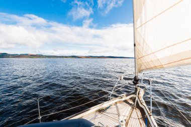 Yağmurdan sonra Tarbert 'in kayalık kıyılarında seyir halindeki ahşap meşe güvertesiyle donatılmış modern bir yat. İskoçya, İngiltere. Güverteden pruvaya, direğe ve yelkenlere yakın görüntü. Dramatik fırtına gökyüzü