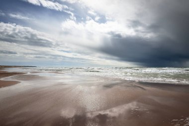 Fırtına sonrası dramatik bulutların altında Baltık Denizi 'nin kumlu sahili. Letonya 'da sızıntı var. Destansı deniz manzarası. Kasırga, fırtına, sert hava, meteoroloji, iklim değişikliği, doğal fenomen
