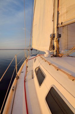 Günbatımında yağmurdan sonra beyaz yat denize açılacak. Güverteden pruvaya kadar yakın çekim. Durgun bir suya yansıyan parlak bulutlarla dolu berrak mavi bir gökyüzü. Idyllic deniz manzarası. Deniz, seyahat, seyahat yerleri