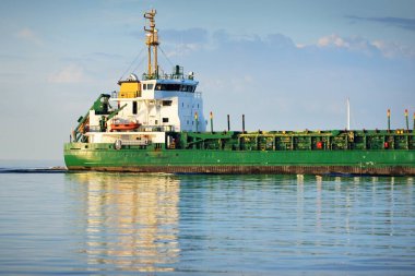Büyük yeşil kargo gemisi gün batımında açık denizde yelken açıyor. Renkli parlayan bulutlar, sıcak güneş ışığı. Görüntüyü algıla. Nakliye, iş, ekonomi, sanayi, küresel iletişim, lojistik