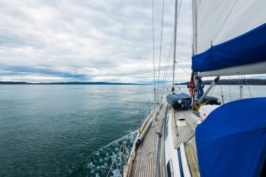 Bulutlu bir günde, Jura adasının kayalık kıyılarında seyir halindeki ahşap meşe güvertesiyle donatılmış modern bir yat. Inner Hebrides, İskoçya, İngiltere. Spor, eğlence, gezi, seyahat yerleri.