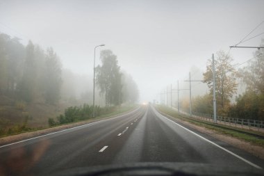 Yoğun siste boş asfalt yolu (karayolu). Elektrik hattı, yakın plan. Kentsel sonbahar manzarası kavramı. Ulaşım, tehlikeli sürüş, hız, özgürlük, seyahat, turizm, yol