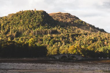 Loch Fyne kıyısındaki görkemli orman tepeleri. Küçük bir yol ve taş köprü. Dramatik gün batımı gökyüzü. Inveraray, Argyll ve Bute, İskoçya, İngiltere. Seyahat hedefleri teması