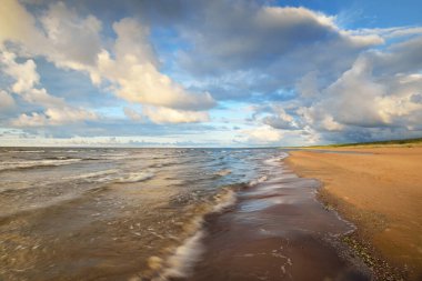 Gün batımında fırtınadan sonra Baltık kıyıları üzerinde parlayan kümülüs bulutlarıyla açık bir gökyüzü. Dramatik bulut manzarası. Sıcak altın güneş ışığı. Resimli bir manzara var. Hava kararsız. Uzun pozlama