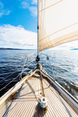 Yağmurdan sonra Tarbert 'in kayalık kıyılarında seyir halindeki ahşap meşe güvertesiyle donatılmış modern bir yat. İskoçya, İngiltere. Güverteden pruvaya, direğe ve yelkenlere yakın görüntü. Açık mavi gökyüzü