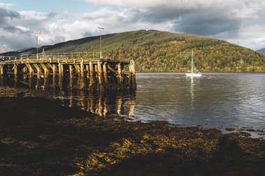 Yelkenli teknesi Loch Fyne kıyısında demirlemiş, yakın mesafeden. Dramatik bir gökyüzü. Arkadaki görkemli orman tepeleri. Inveraray, Argyll ve Bute, İskoçya, İngiltere. Seyahat hedefleri teması