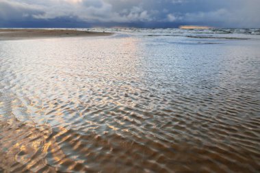 Gün batımında Baltık Denizi 'nin panoramik manzarası. Koyu renkli kümülüs bulutlarıyla dramatik bir gökyüzü. Su yüzeyi dokusu yakın çekim. Kararsız hava, kış, iklim değişikliği, doğa, çevre