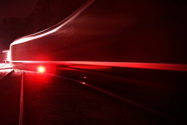 Terminalden gece ayrılan büyük kargo treni, vagonlar (konteynırlar) yakın çekimde. Şehir manzarasını düşün. Aydınlanma, kırmızı ışık, hareket bulanıklığı. Nakliye, endüstri, lojistik