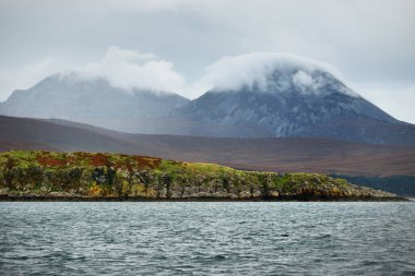 Jura adasının kıyılarının panoramik manzarası, dağları ve vadileri sudan. Bulutlu mavi gökyüzü. Fırtınalı hava. Paps of Jura, Inner Hebrides, İskoçya, İngiltere
