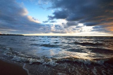 Gün batımında fırtınadan sonra Baltık Denizi kıyısında bir sürü koyu renkli kümülüs bulutu olan açık bir gökyüzü. Dramatik bulut manzarası. Sıcak altın ışık. Resimli bir manzara var. Kararsız hava, iklim değişikliği