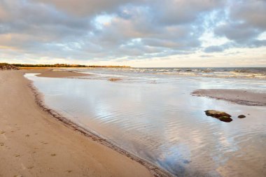 Kumlu bir sahilden Baltık Denizi 'nin panoramik manzarası. Açık günbatımı gökyüzü, parlak pembe bulutlar, yumuşak ışık. Suyun simetri yansımaları, doğal ayna. Hava, kış, iklim değişikliği, doğa
