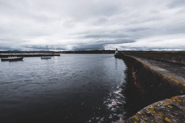 Eski deniz fenerine doğru boş bir gezinti, yakın plan. Arka planda kayalık kıyılar var. Dramatik bulut manzarası. Ardrishaig, Crinan Kanalı, İskoçya, İngiltere. Seyahat yerleri, gezi teması