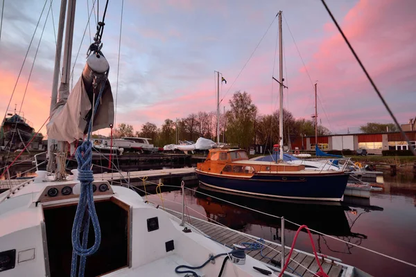 Elegant and modern sailing boats (for rent) moored to a pier in a yacht marina at sunset. Sweden. Colorful sky with glowing pink clouds. Vacations, sport, amateur recreational sailing, cruise