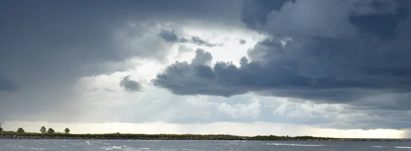 Clear sky with lots of dark glowing cumulus clouds above the Baltic sea shore after thunderstorm at sunset. Dramatic cloudscape. Panoramic view. Fickle weather, seasons, climate change