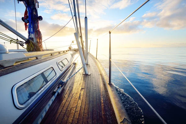 Sloop rigged modern yacht with wooden teak deck sailing at sunrise. Colorful clouds is reflecting in the water. Port Ellen, Isle of Islay, Inner Hebrides, Scotland, UK