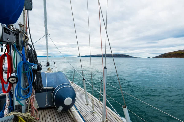 Sloop rigged modern yacht with wooden teak deck sailing near the rocky shore of Jura island on a cloudy day, close-up. Inner Hebrides, Scotland, UK. Sport, recreation, cruise, travel destinations