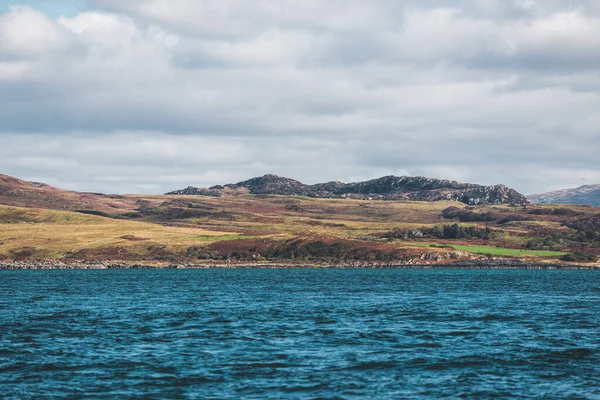 Sailing near the rocky shores (cliffs) of the west coast of Jura island, a view from the yacht. Dramatic sunset sky with glowing clouds. Inner Hebrides, Scotland, UK. Travel destinations, landmarks