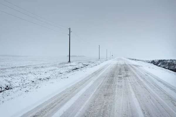 吹雪の後 フィールドを介して雪に覆われた田舎道 送電線 変圧器の棒 車からのパノラマビュー 暗い嵐の空 オフロード 冬のタイヤ リモート村 — ストック写真