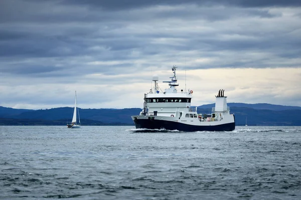 Jura adasının batı kıyısındaki kayalık kıyılarda yelken açan küçük bir gemi, yattan bir manzara. Fırtınadan sonra dramatik bulutlar. Inner Hebrides, İskoçya, İngiltere. Atmosferik manzara