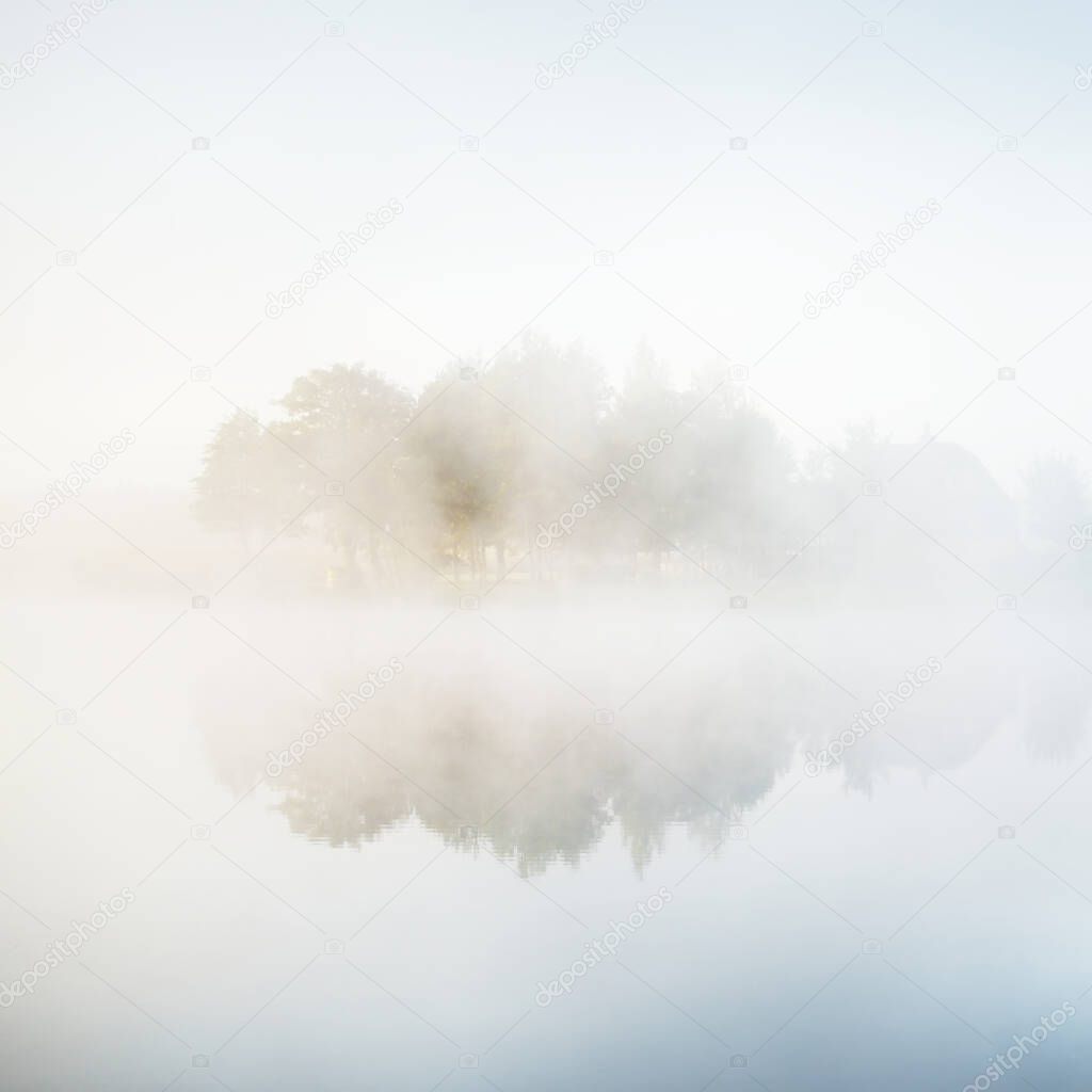 Picturesque scenery of the forest lake in a thick white fog. Reflections on the water. Pure golden sunlight. Atmospheric landscape. Fall season. Nature, ecology, environmental conservation in Europe